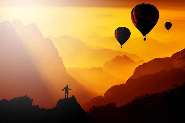 Silhouetted of man standing on mountain with hot-air balloons fl