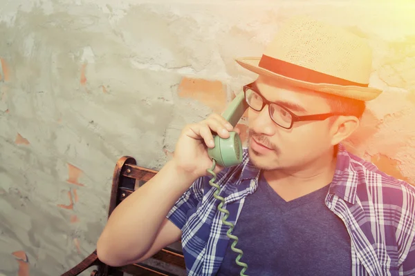 Handsome hipster man talking with retro phone on the brick backg