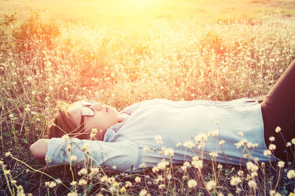 Happy hipster woman lying down on dandelion field close her eyes