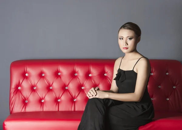 Beautiful woman in black dress sitting on red sofa