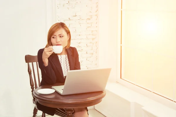Business woman drinking coffee and using laptop  in office