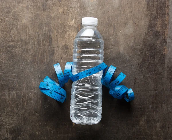 Plastic bottle of water with measuring tape over the wooden back
