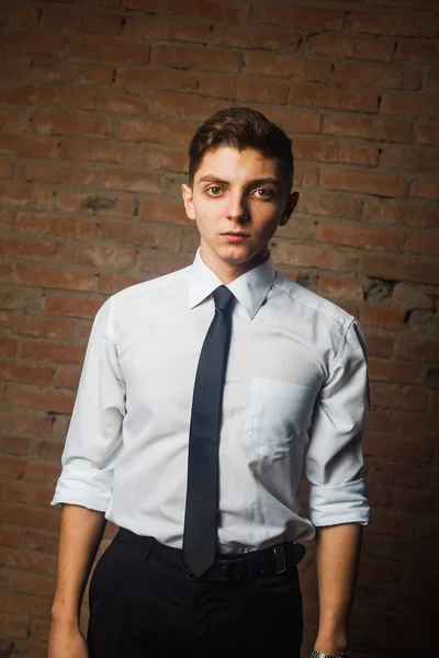 Fashionable handsome young male model posing in front of a white brick wall.