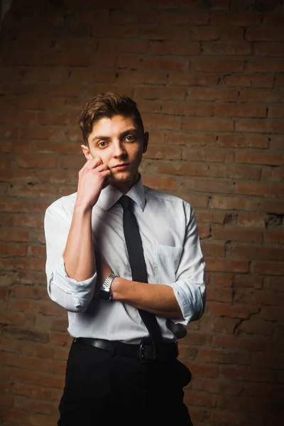 Fashionable handsome young male model posing in front of a white brick wall.