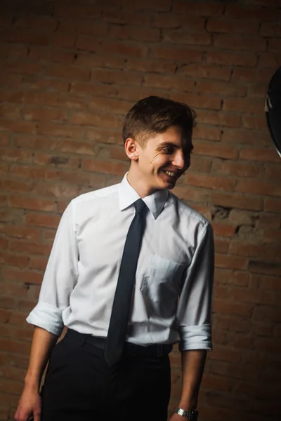 Fashionable handsome young male model posing in front of a white brick wall.