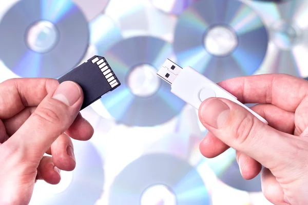 Man's hands with SD card and pendrive over CD's background. Conc