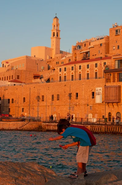 Israel: children fishing at the port of Jaffa with view of the Old City at sunset