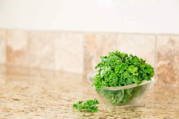 A bowl of fresh green kale on a granite countertop