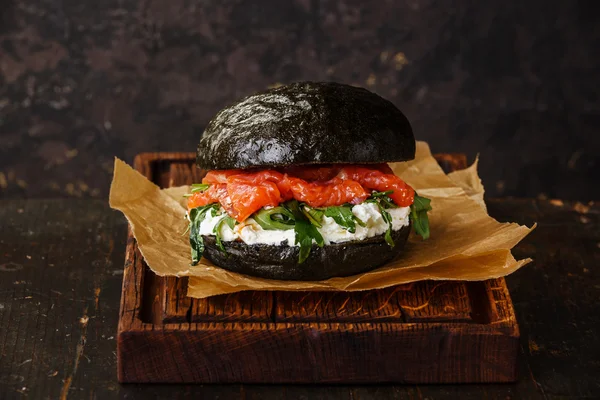 Black Salmon burger with cream cheese and arugula on dark wooden