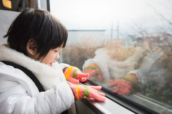 Happy asian child looking out train window outside