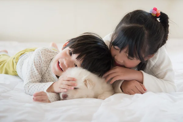 Children and puppy having fun lying in bed