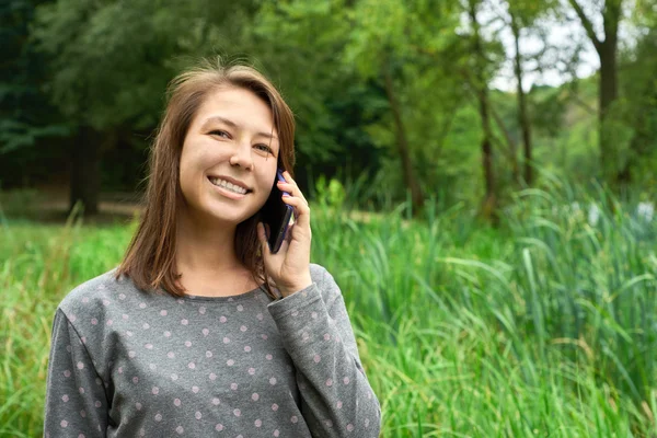 Happy young woman speaks on the phone in the forest