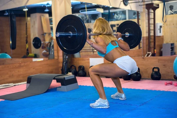Women squats with a barbell in the gym