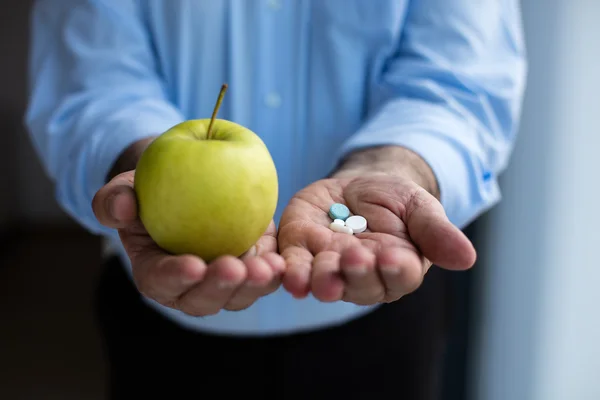 Old hand holding pills and apple