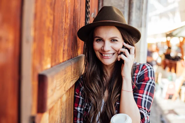 Young woman with a hat next to an old wooden door talking at cel