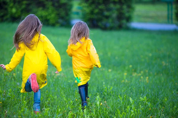 Funny cute toddler girls wearing waterproof coat playing outdoors by rainy and sunny day