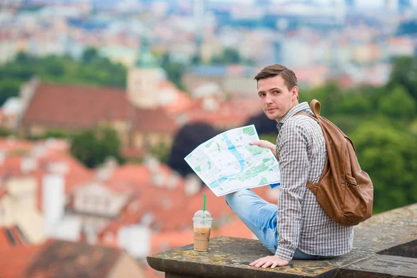 Young man with a city map and backpack background european city. Caucasian tourist looking at the map of European city with beautiful view of attractions.