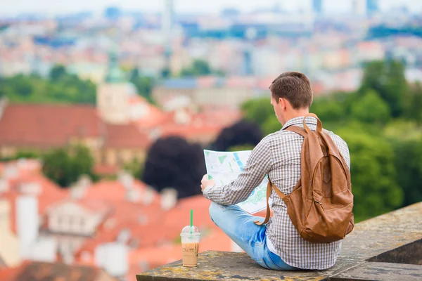 Young man with a city map and backpack background european city. Caucasian tourist looking at the map of European city with beautiful view of attractions.