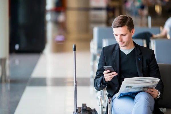 Passenger in an airport lounge waiting for flight aircraft. Young man with cellphone in airport waiting for landing
