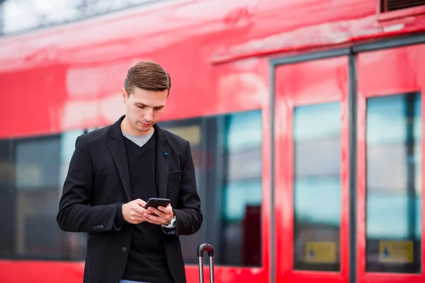 Young caucasian man with smarphone and luggage at station traveling by train