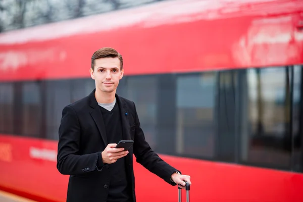 Young caucasian man with smarphone and luggage at station traveling by train