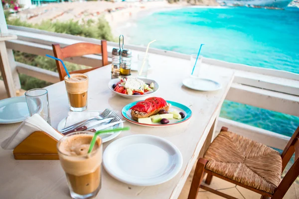 Traditional dinner with delicious fresh greek salad, frappe and brusketa served for lunch at outdoor restaurant with beautiful view on the sea and port