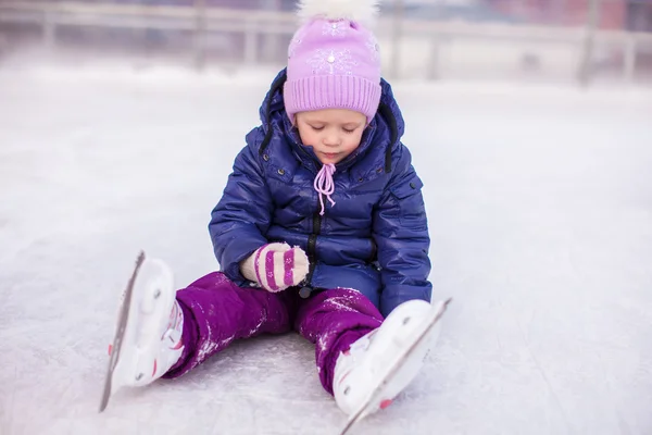 Adorable little girl sitting on ice with skates after the fall