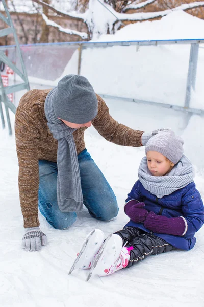 Adorable little girl and happy dad on skating rink outdoor