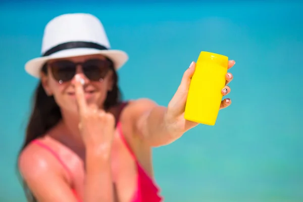 Young happy woman applying suntan lotion on her nose on white beach