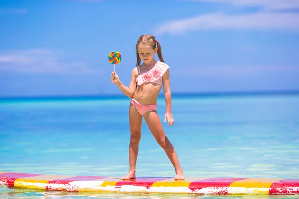 Little girl with lollipop have fun on surfboard in the sea