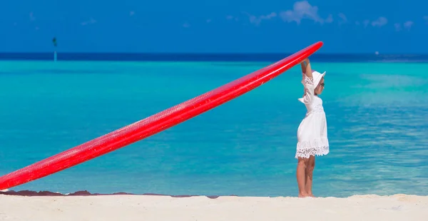 Adorable little girl with red big surfboard during tropical vacation