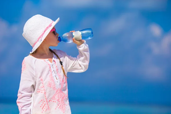 Little girl drinking mineral bottle of water at hot summer day on beach
