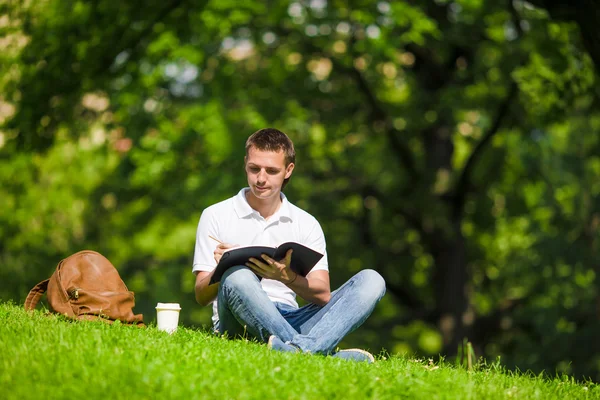 University student studying for exams outdoors in the park. With him his books, notebook, backpack and coffee.