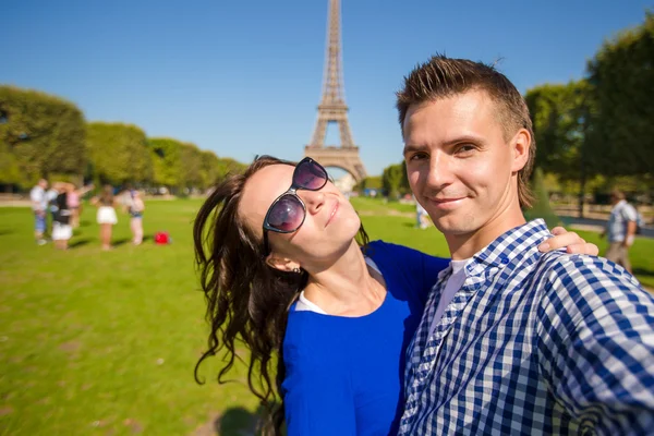 Young happy family taking self portrait in Paris background the Eiffel Tower. Young adults holding smartphone camera to take a picture of themselfes during summer vacation in Europe