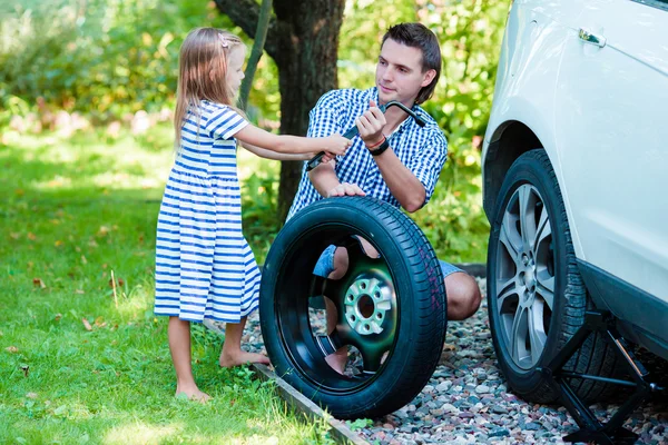 Adorable little girl helping father to change a car wheel outdoors on beautiful summer day