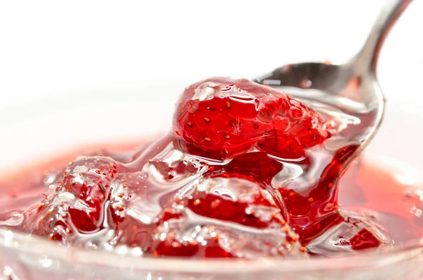 Strawberry jam is stirred with a spoon on a white background. Fruit dessert close up. Confectionery.