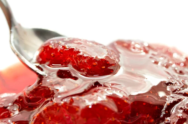 Strawberry jam is stirred with a spoon on a white background. Fruit dessert close up. Confectionery.