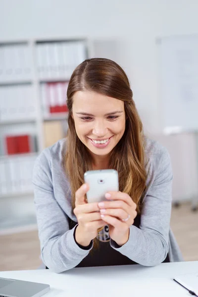 Happy woman looking at cell phone in office