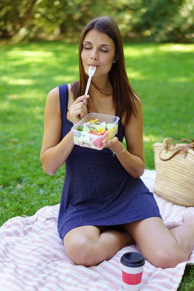 Cute young woman sitting on towel eating
