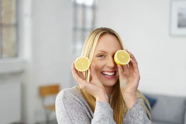 Laughing woman holds a lemon to her eye