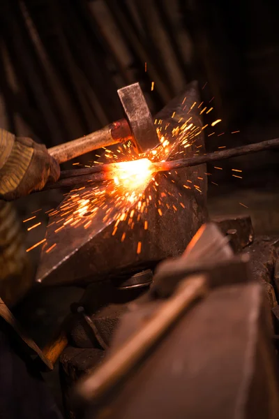 Blacksmith shaping a hot piece of iron on an anvil with a hammer