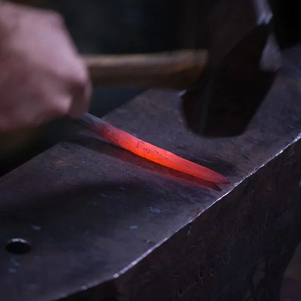 Ironworker forging hot iron in workshop