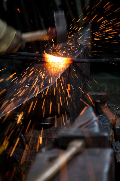 Blacksmith shaping a hot piece of iron on an anvil with a hammer