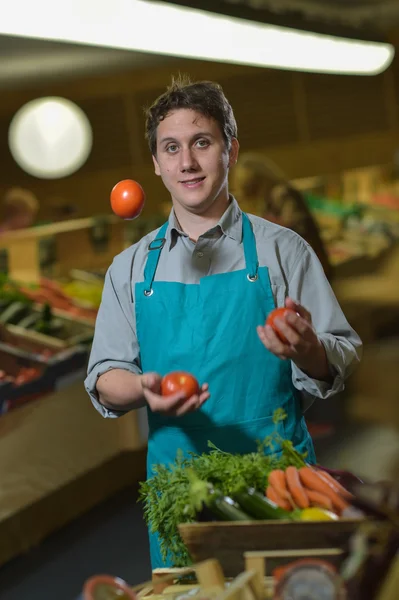 Grocery clerk juggling with tomatoes in supermarket store