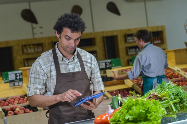 Grocery store employee reading inventory list on digital tablet