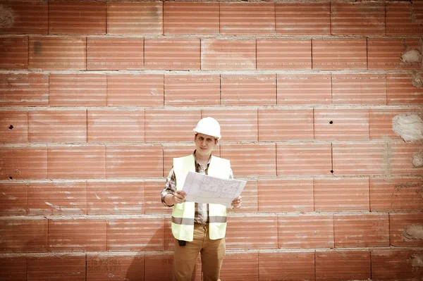 Engineer builder in front of orange brick wall with plan