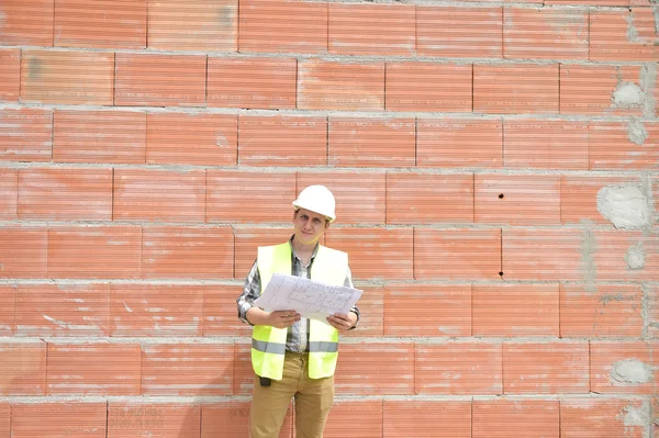 Engineer builder in front of orange brick wall with plan
