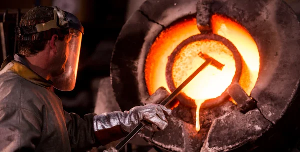 Steel worker in protective clothing raking furnace in an industr