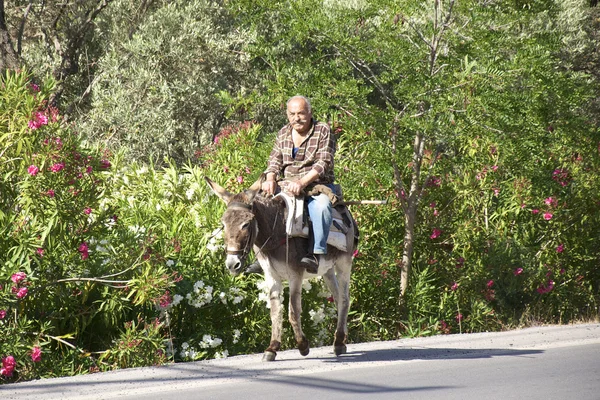 Old man riding a donkey on the street on Crete