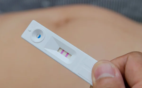 Holding positive pregnancy test with two red stripes